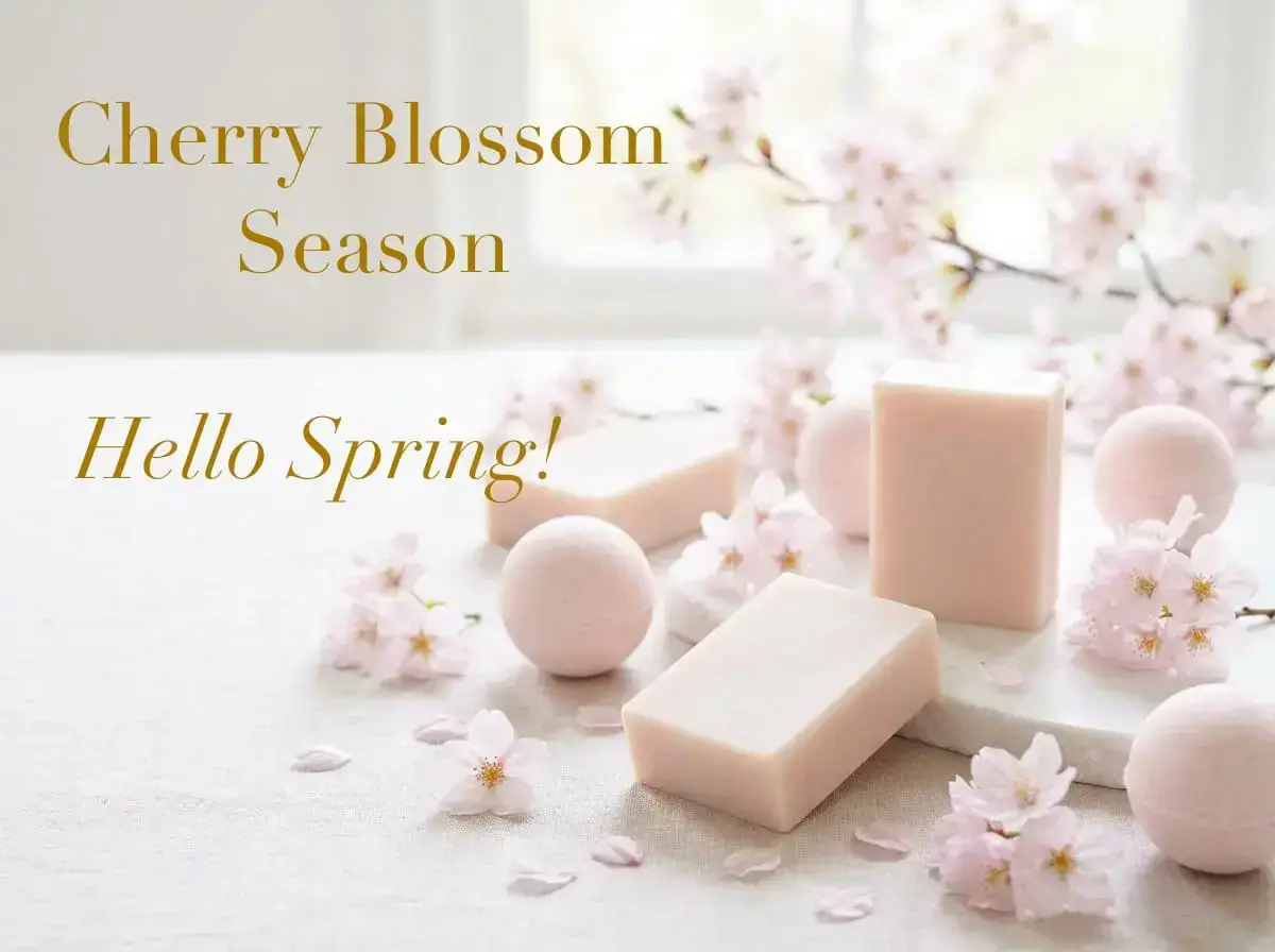 Soft pink soaps and spheres surrounded by cherry blossoms on a white surface, with text "Cherry Blossom Season" and "Hello Spring!" in elegant script.